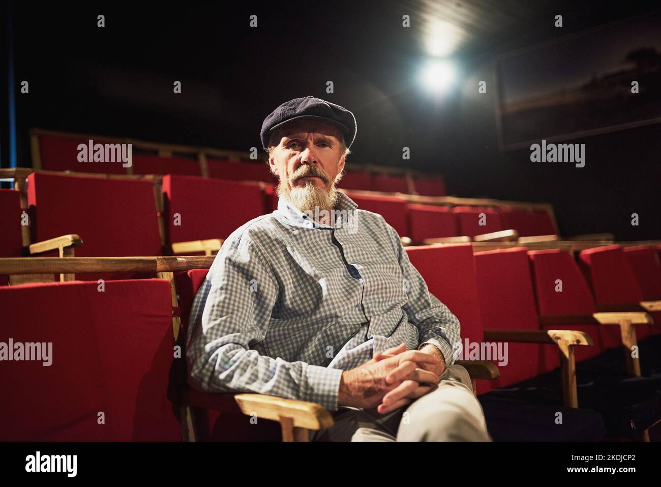 HES un cinephile condito. Ritratto di un uomo anziano sicuro seduto da solo in un cinema vuoto. Foto Stock