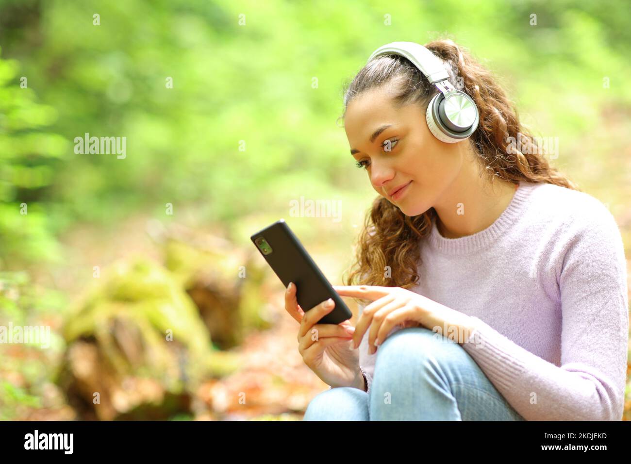 Donna rilassata che indossa cuffie per ascoltare musica e ascoltare i contenuti del telefono in una foresta Foto Stock