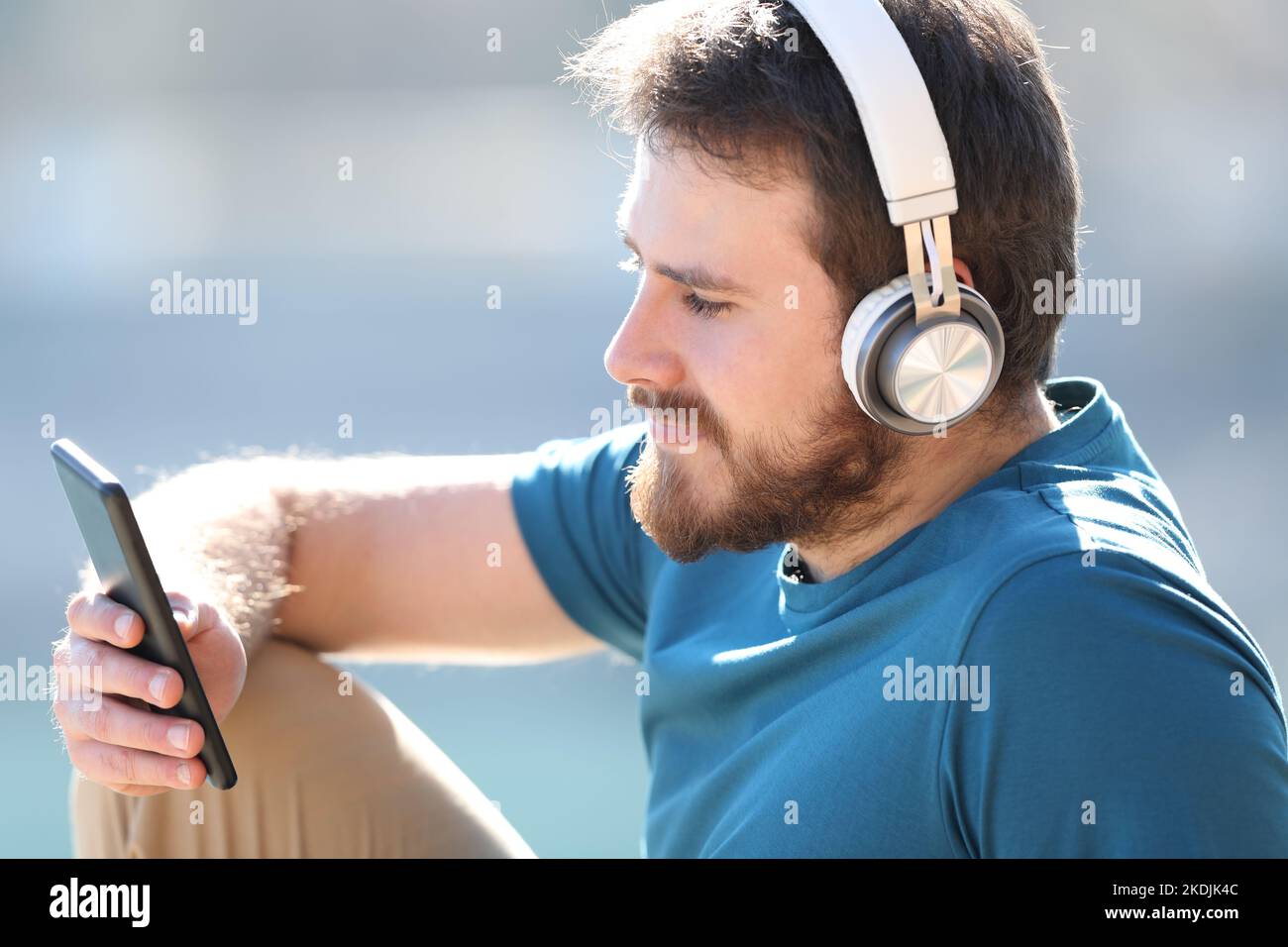 Uomo che indossa le cuffie per ascoltare la musica guardando i contenuti dello smartphone Foto Stock
