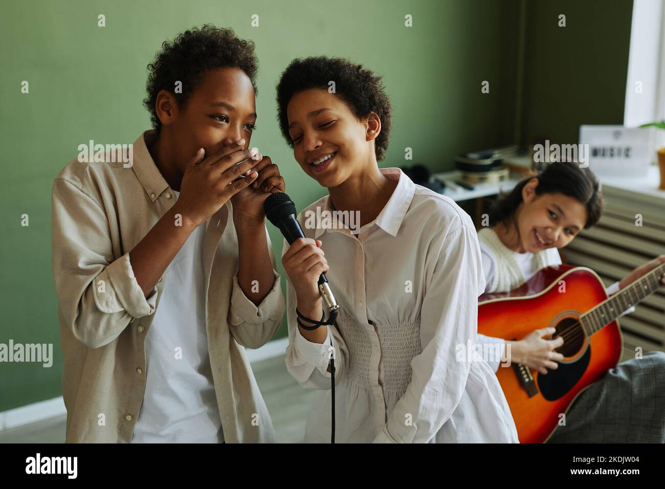 Giovani scolari che suonano canzoni insieme durante la ripetizione con accompagnamento di chitarra acustica suonata da una studentessa asiatica Foto Stock