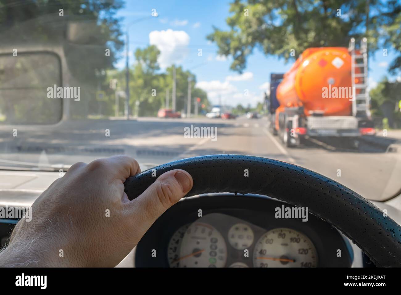 vista della mano del conducente dietro il volante di un'auto che sorpassa un autocarro cisterna con un serbatoio di carburante infiammabile all'incrocio di una strada cittadina Foto Stock