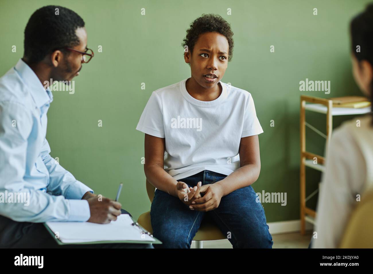 Pre-teen infelice studentessa descrivendo il suo problema al compagno di classe mentre si siede di fronte alla studentessa afroamericana e allo psicologo scolastico Foto Stock
