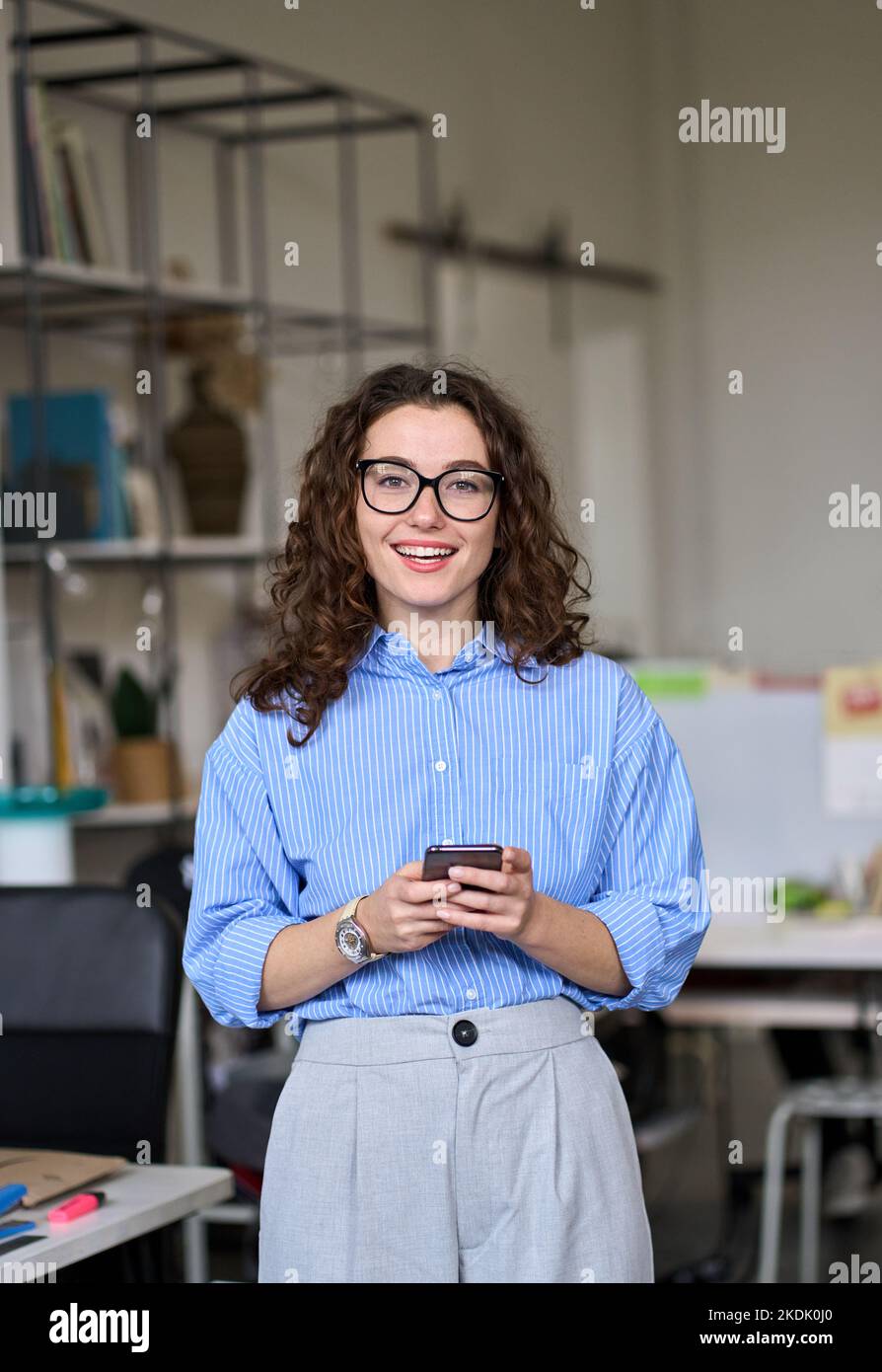 Felice giovane donna d'affari che tiene il telefono in piedi in ufficio, verticale. Foto Stock