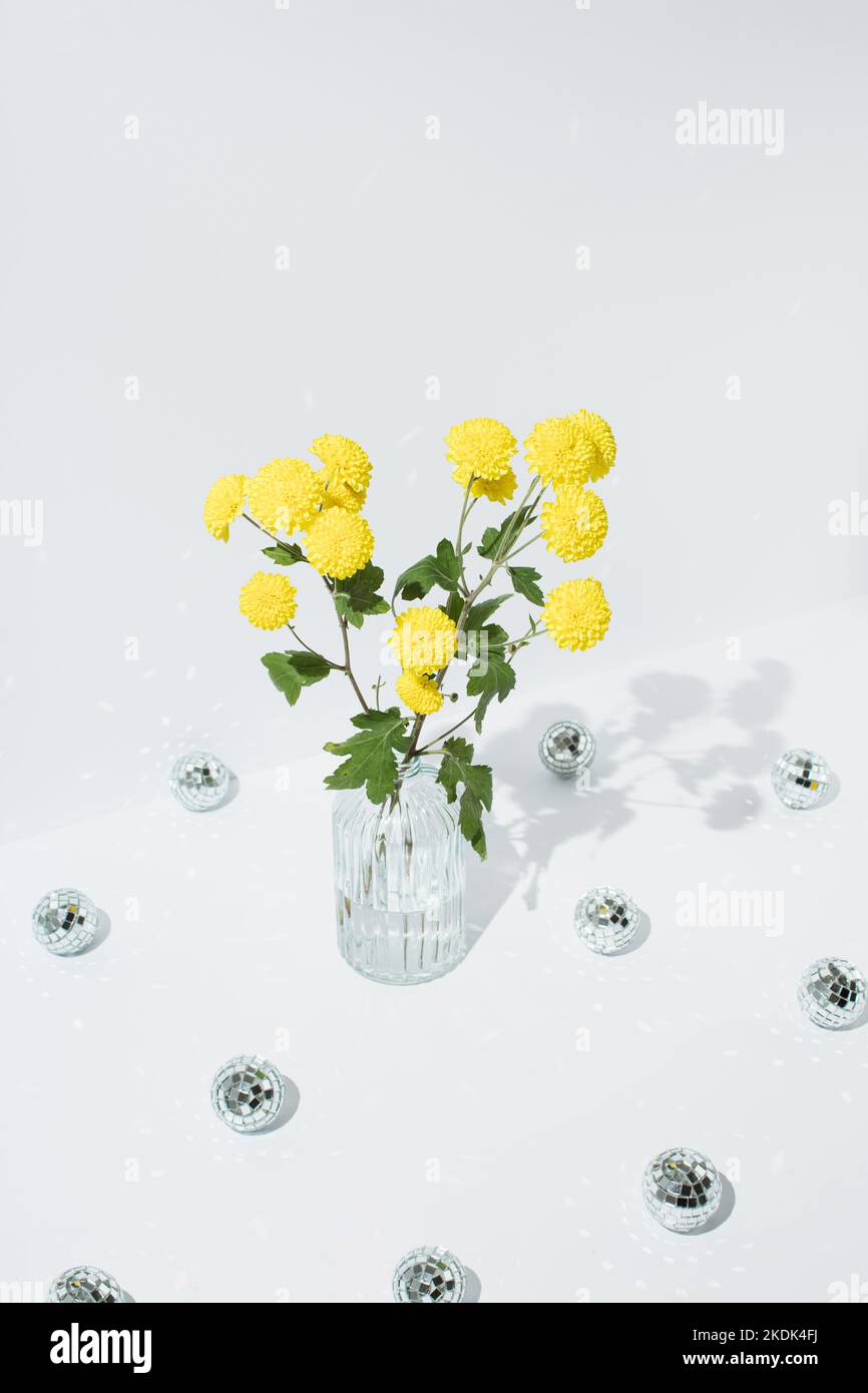 Bouquet di fiori gialli in vaso con palline da discoteca lucenti sparse su sfondo bianco. Concetto minimo. Foto Stock