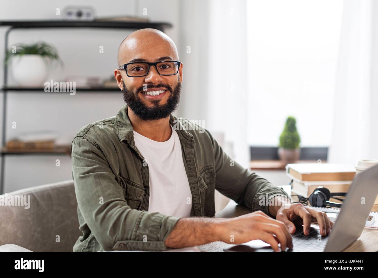 Ritratto di felice uomo latino maturo seduto alla scrivania, lavorando su pc portatile e sorridendo alla fotocamera, spazio libero Foto Stock
