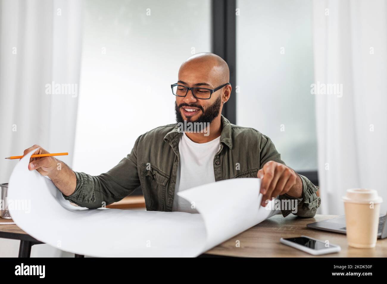 Felice ingegnere industriale latino maturo guardando i disegni di progetto lavoro a tavola, lavorando all'interno di ufficio, copia spazio Foto Stock