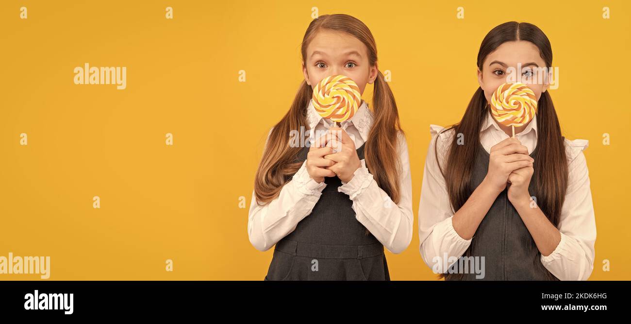 I bambini della scuola affamati tengono le lollipops colorate di swirl su sfondo giallo bastoni. Bambino adolescente con dolci, intestazione banner poster, spazio copia. Foto Stock