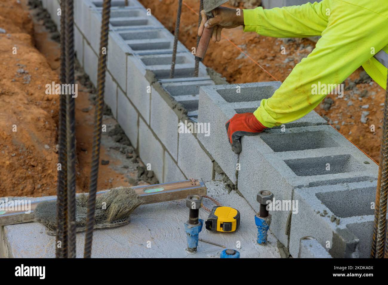 Lavoratore di costruzione che posa un'altra fila di blocchi di cemento su terra da muratore Foto Stock