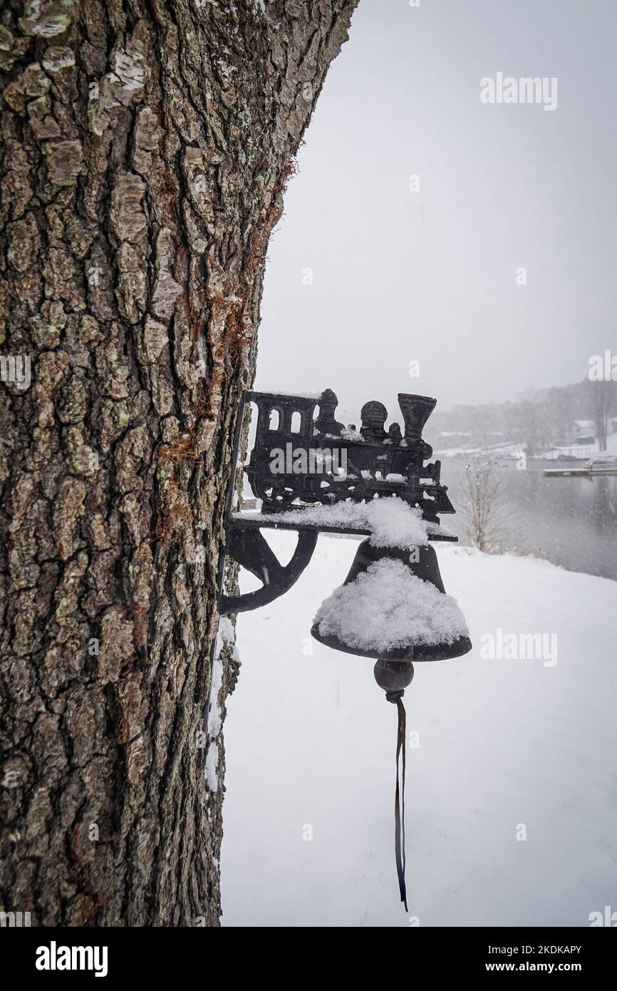 Neve su un antico campanello in ghisa appeso ad un albero in inverno. Foto Stock
