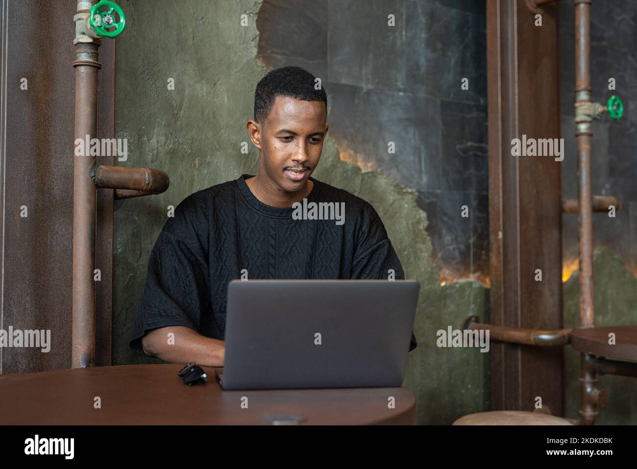 Ritratto di un bell'uomo nero seduto e che utilizza un computer portatile in interni Foto Stock
