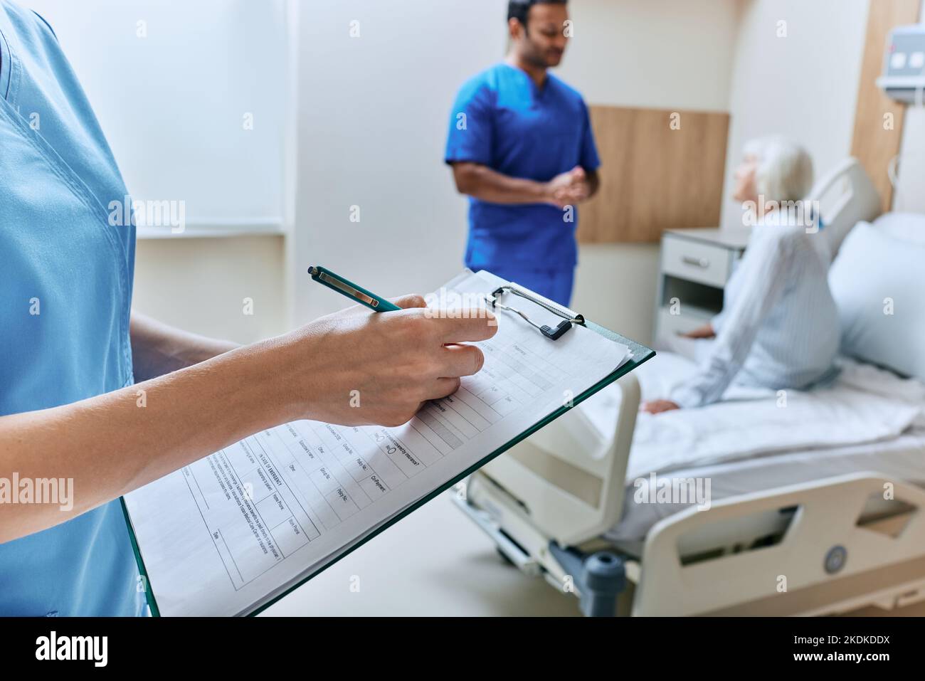 L'infermiere prende appunti nella cartella clinica nella stanza dell'ospedale con paziente anziano e medico durante la consultazione al posto letto. cura medica per il paziente Foto Stock