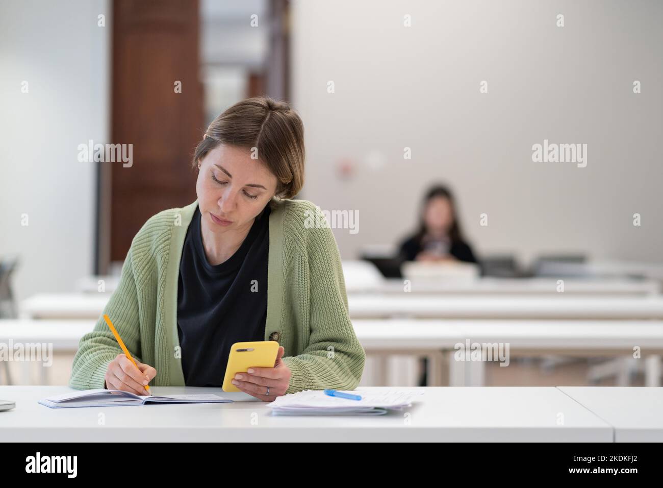 Studentessa matura concentrata utilizzando lo smartphone per la preparazione dell'esame, ottenendo il secondo grado Foto Stock