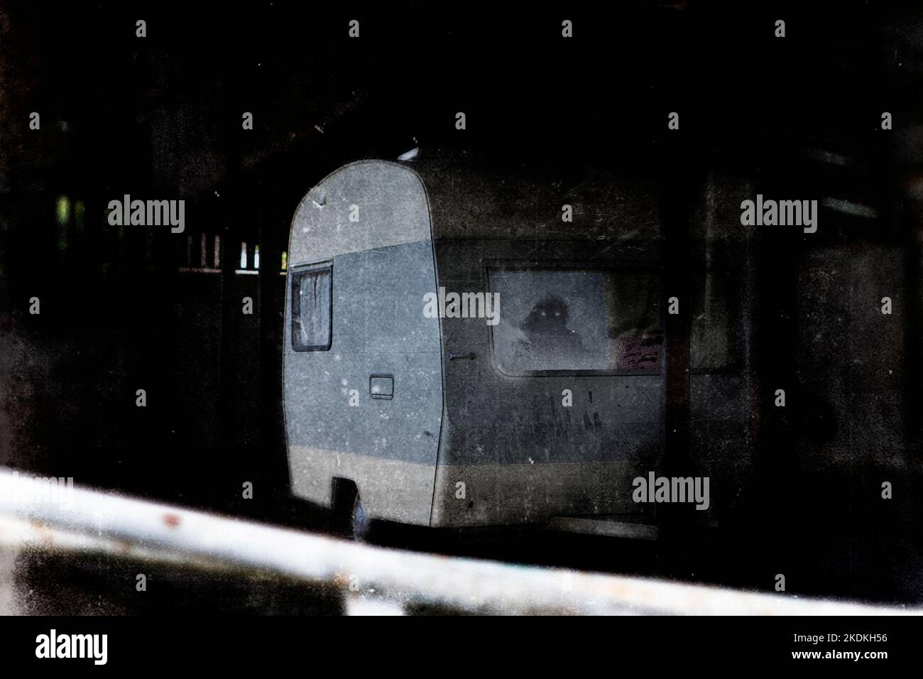 Un concetto orrore di una carovana abbandonata in un edificio spaventoso e derelitto. Con un fantasma con occhi luminosi che guardano fuori. Con un grunge, texture edit. Foto Stock