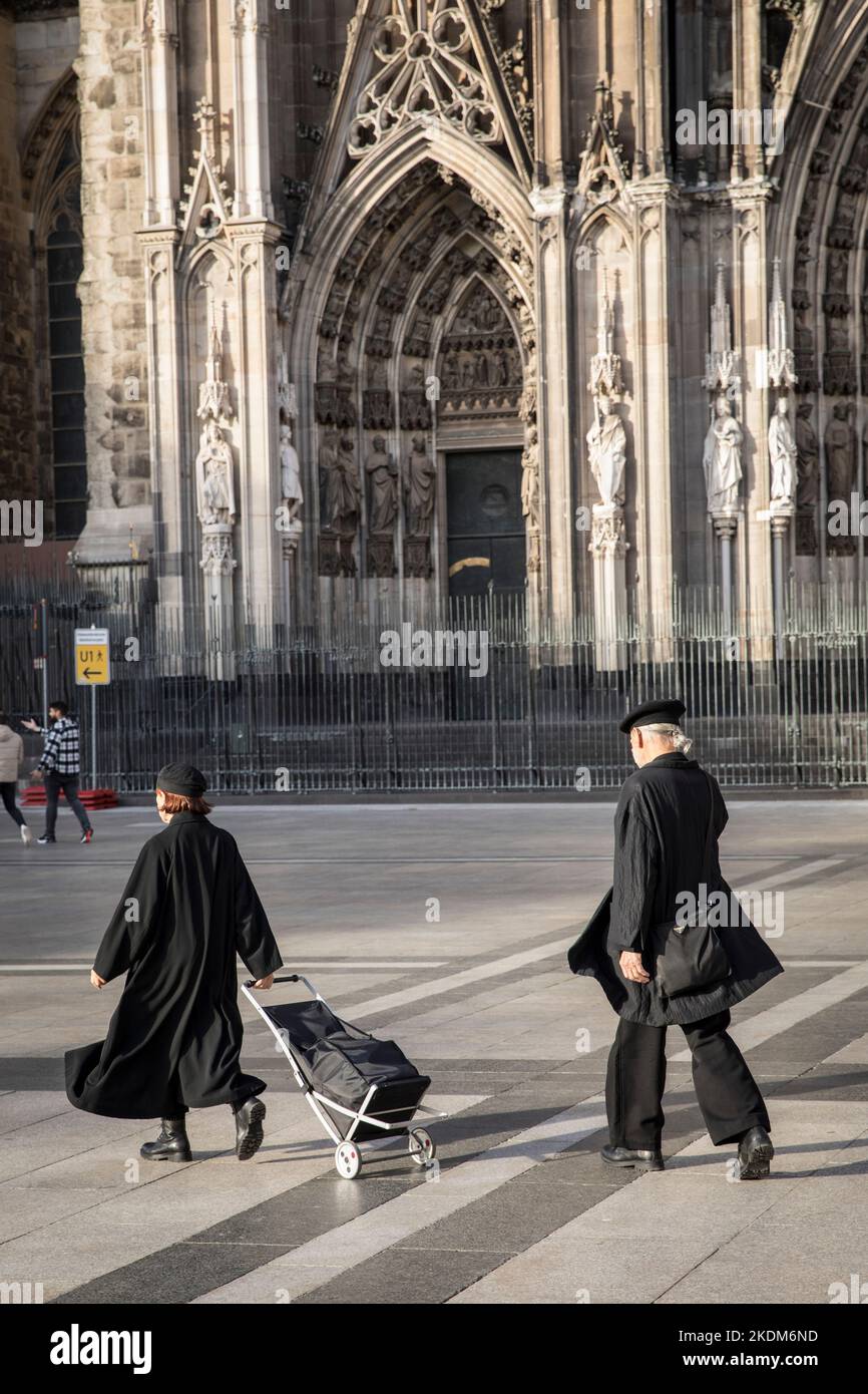 Una coppia anziana vestita di nero con un tram nero attraversa Roncalliplatz alla cattedrale di Colonia, Germania. ein aelteres Paar ganz in schwar Foto Stock