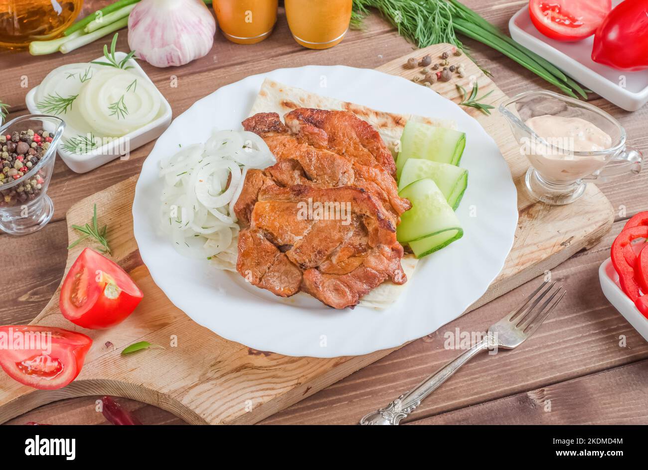 Spiedini di carne di maiale con cipolle e verdure fresche su un piatto bianco su uno sfondo di legno scuro. Foto Stock