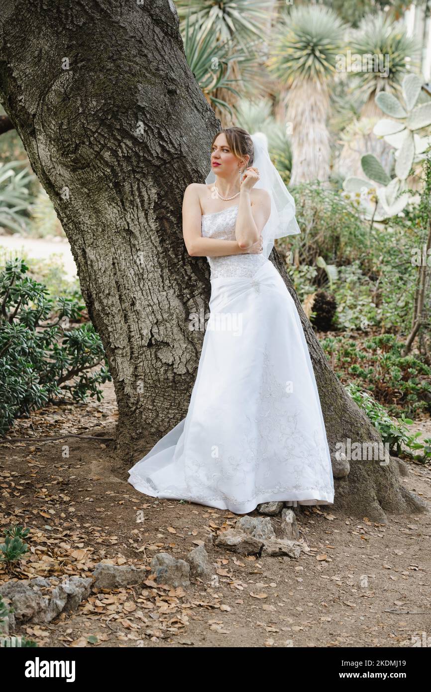 Sposa che si appoggia contro l'albero di quercia in un giardino di Cactus Foto Stock