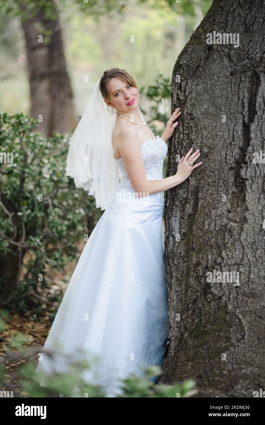 Sposa che si appoggia contro l'albero di quercia in un giardino di Cactus Foto Stock