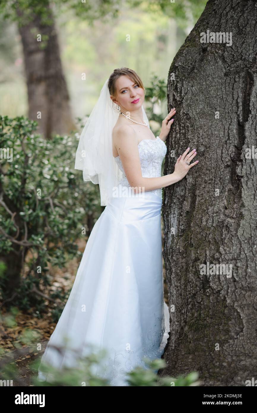 Sposa che si appoggia contro l'albero di quercia in un giardino di Cactus Foto Stock