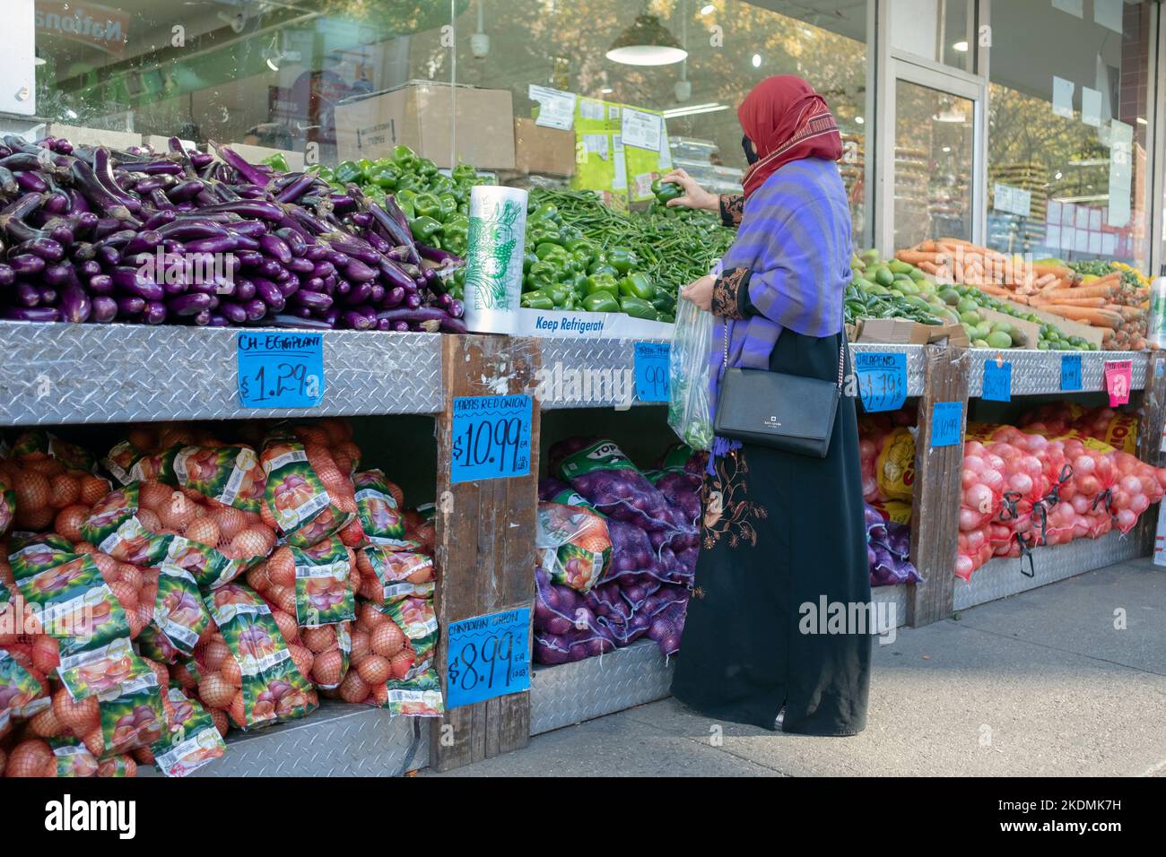 Una donna musulmana in negozi di abbigliamento modesti tradizionali per i peperoni in uno stand il supermercato Apna sul viale 37th a Jackson Heights, Queens, New York. Foto Stock