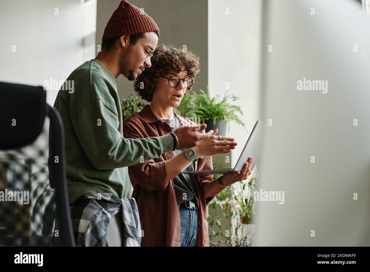 Due giovani programmatori interculturali che discutono dei dati online e esprimono il punto di vista sul video che descrive lo sviluppo di software Foto Stock