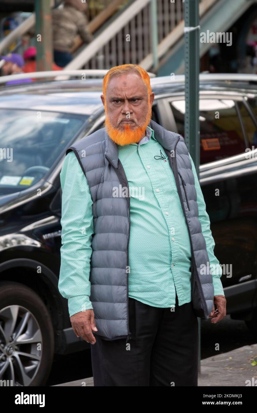 Un venditore, probabilmente del Bangladesh, con i capelli e la barba tinti di arancione. Sulla 74th Street a Queens, New York. Foto Stock