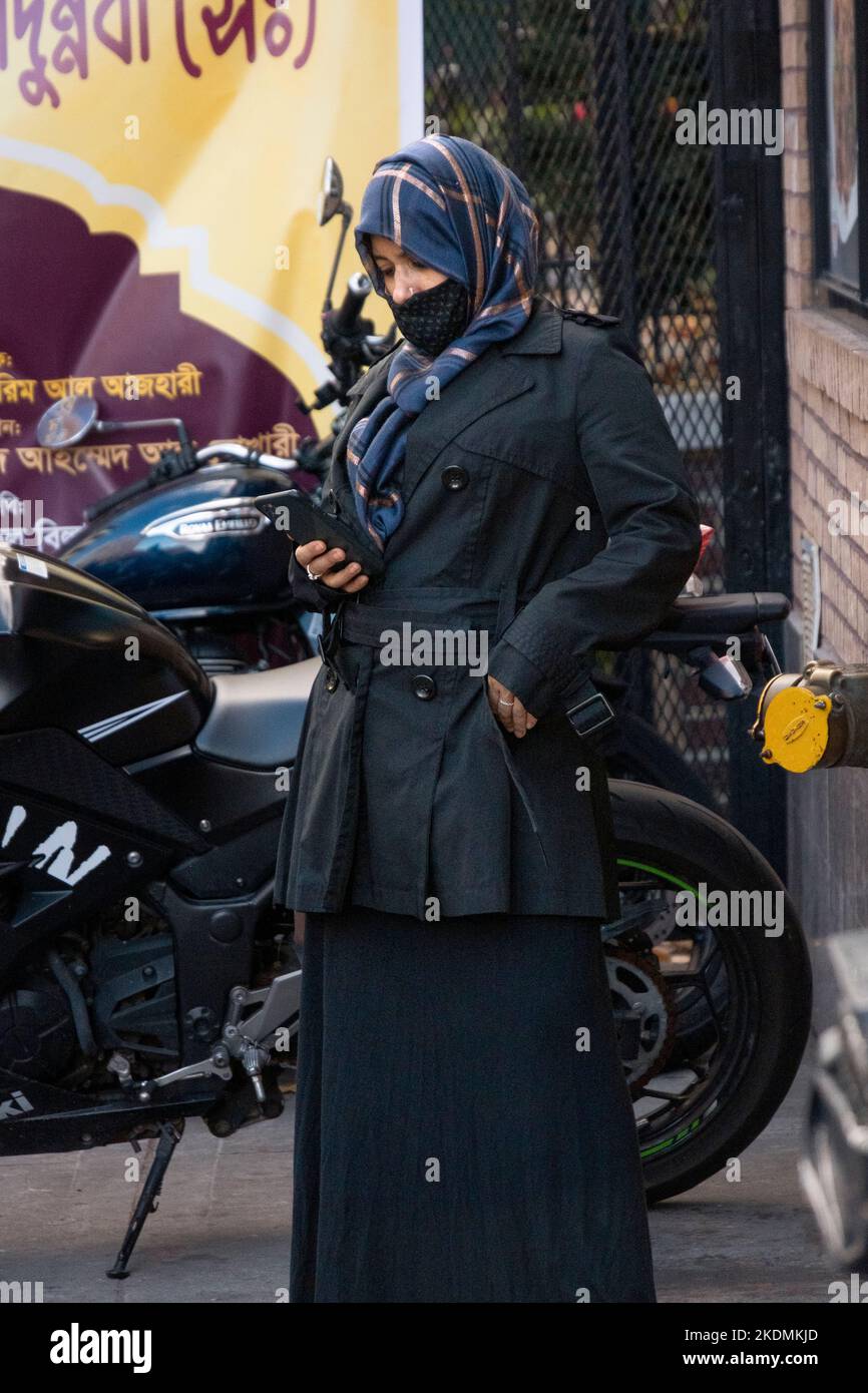 Una donna musulmana in un hijab legge dal suo telefono delle cellule. A Jackson Heights, Queens, New York. Foto Stock