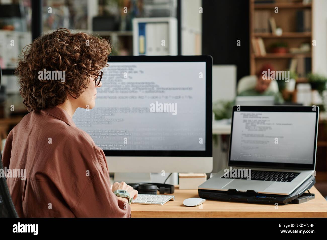 Un giovane INGEGNERE IT che guarda lo schermo del notebook con dati codificati e li decodifica mentre sviluppa un nuovo software nello spazio di coworking Foto Stock