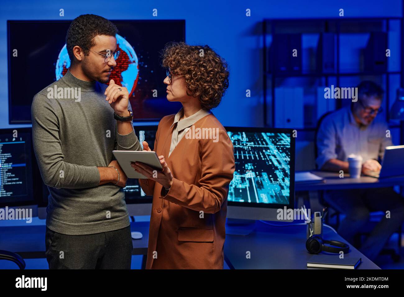 Due programmatori giovani e sicuri discutono idee per un nuovo progetto creativo mentre una donna con un tablet fa la presentazione di alcuni punti Foto Stock