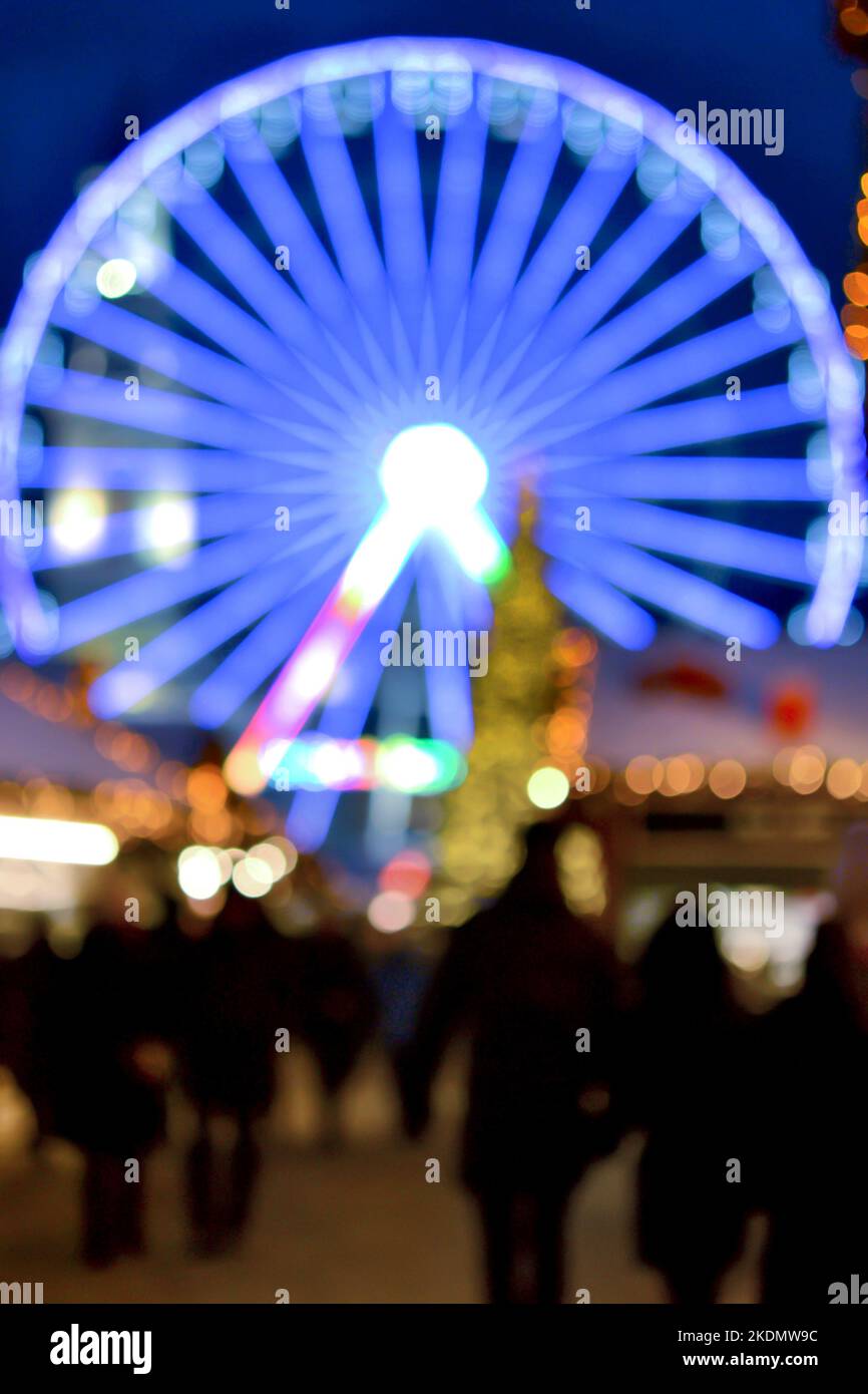 Ruota panoramica decorata con illuminazione blu, albero di Natale, silhouette nere di persone che camminano, edifici cittadini nella notte d'inverno. Città di Natale. Bella vacanza di Natale di Capodanno sfondo sfocato Foto Stock