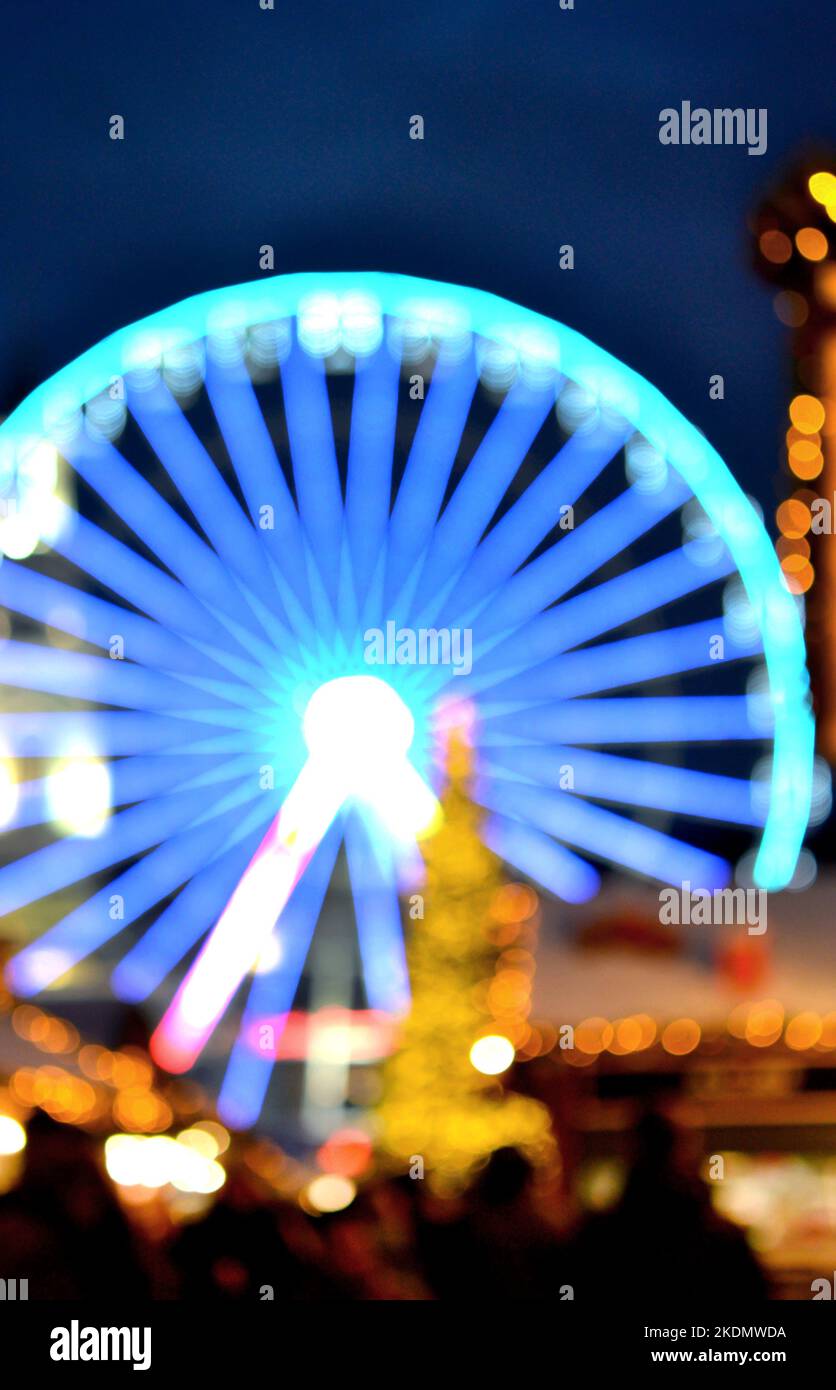 Ruota panoramica decorata con illuminazione blu, albero di Natale, silhouette nere di persone che camminano, edifici cittadini nella notte d'inverno. Città di Natale. Bella vacanza di Natale di Capodanno sfondo sfocato Foto Stock