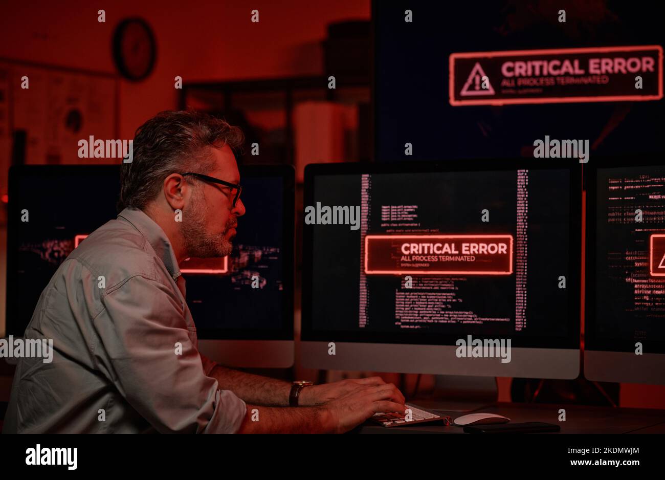 Vista laterale di un responsabile del supporto IT maturo che cerca di risolvere problemi tecnici seduti davanti agli schermi del computer con errori critici Foto Stock