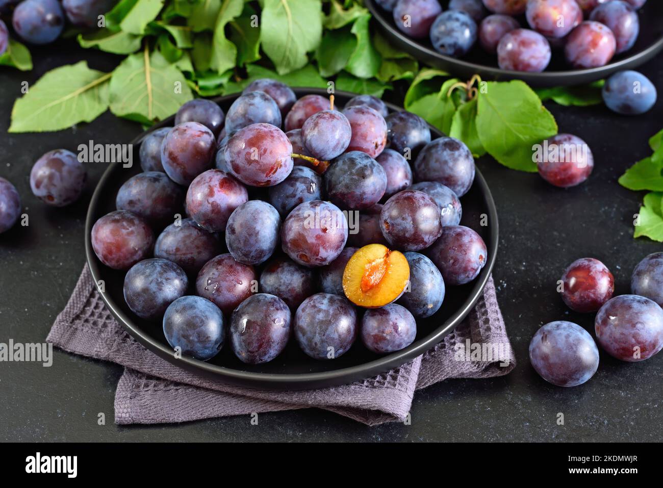 Prugne fresche su piatto su fondo di pietra scura Foto Stock