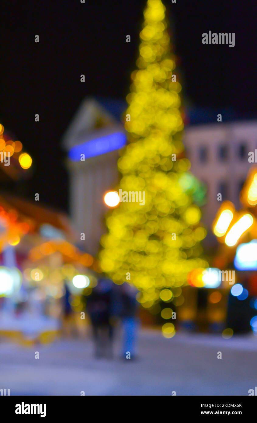 Sfondo sfocato. Albero di Natale, luci decorate, edificio, sagome sfocate di persone che camminano piazza della città durante la notte d'inverno. Bello Capodanno e Natale vacanza sfondo sfocato Foto Stock