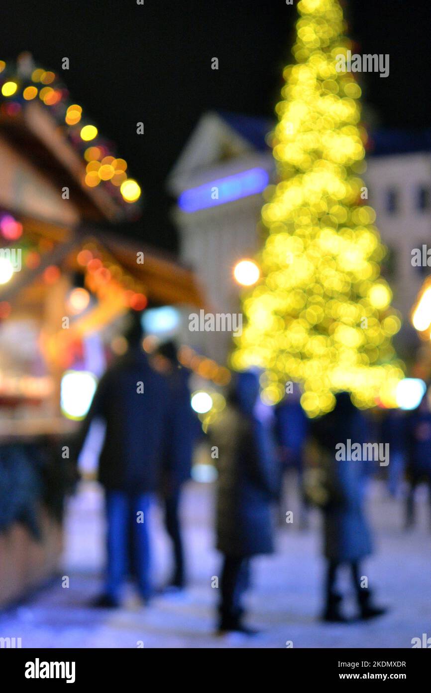 Sfondo sfocato. Albero di Natale di Capodanno decorato giallo ghirlande illuminazione, piccole case di legno ghirlande sul tetto e sagome di persone che camminano lungo la strada della città. Video verticale Foto Stock