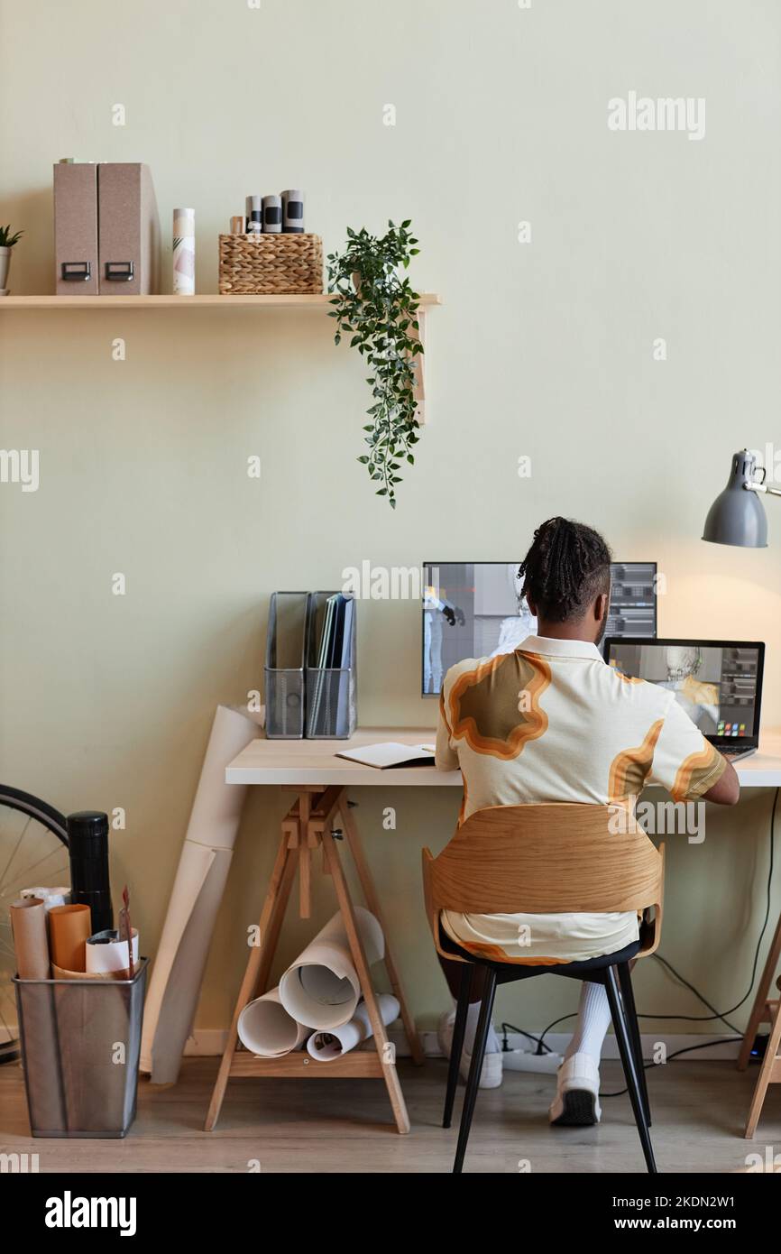 Vista posteriore verticale di un uomo nero creativo che costruisce modelli 3D digitali sul luogo di lavoro dell'ufficio domestico Foto Stock