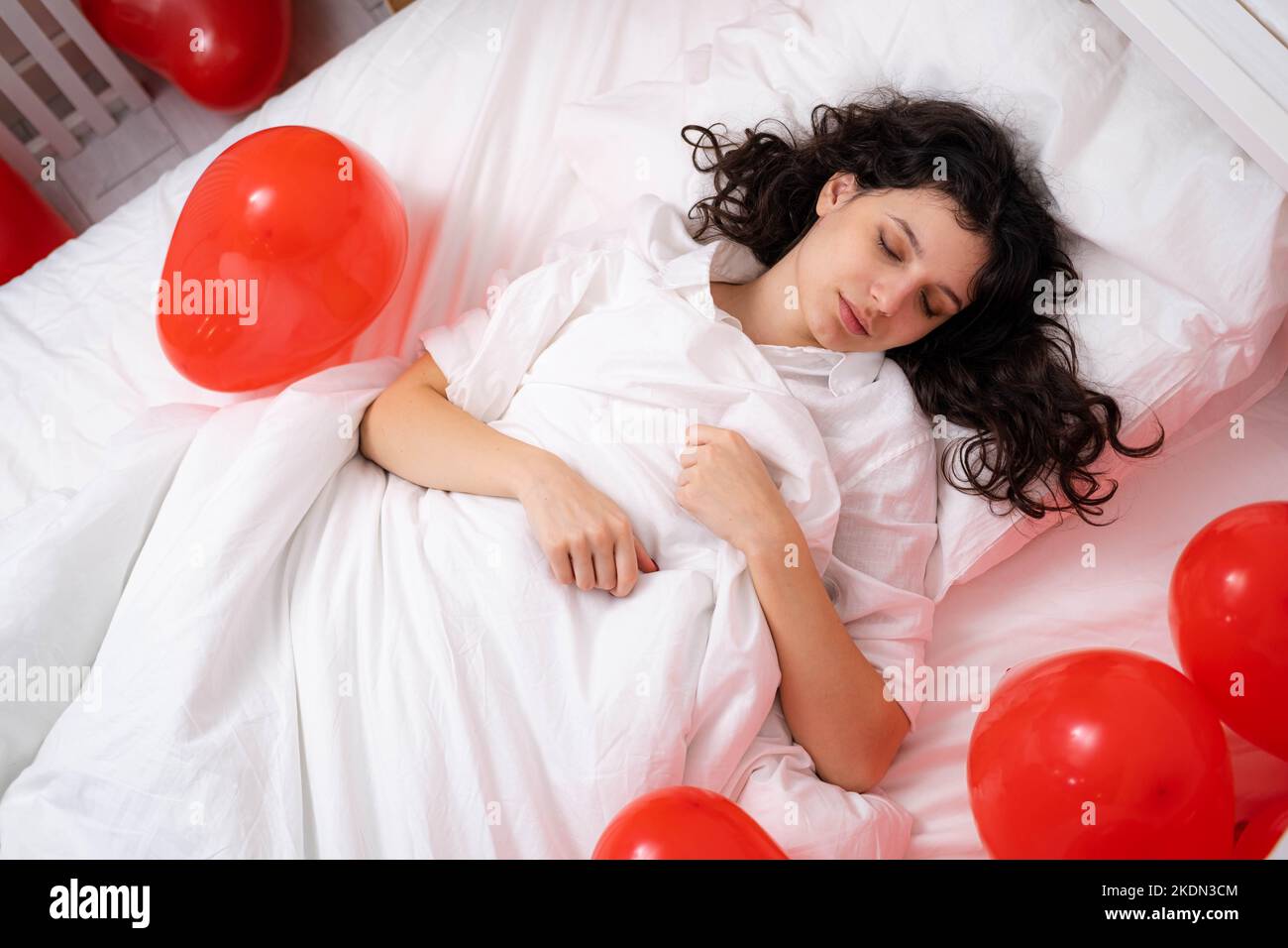 Brunette europea ragazza che dorme a letto con cuore rosso forma palloncini.Morning sorpresa regalo il giorno valentines Foto Stock