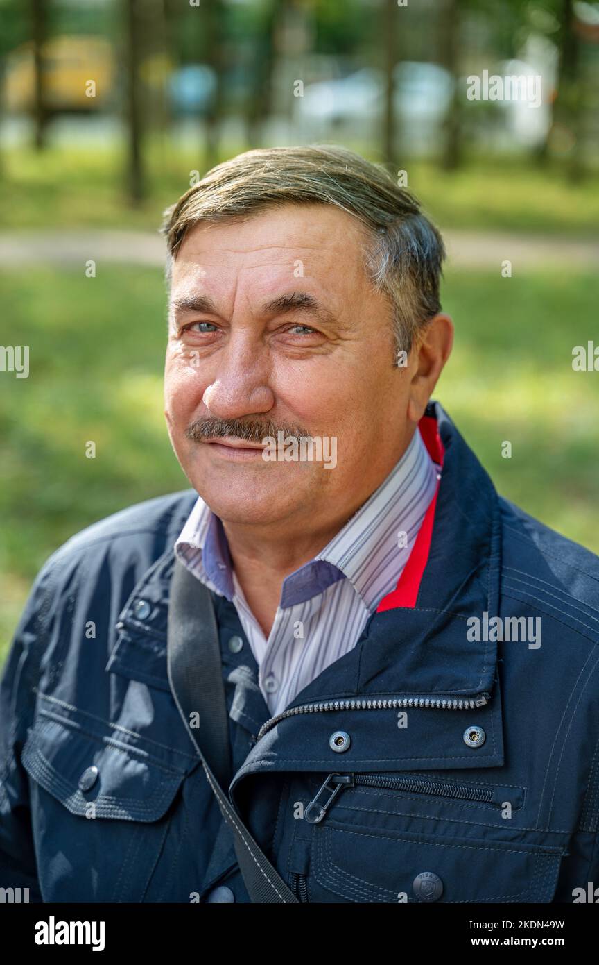 l'anziano uomo di 70 anni riposa seduto su una panchina in autunno. L'uomo sorride guardando la telecamera. Ottimismo e fiducia nell'età adulta. Foto Stock