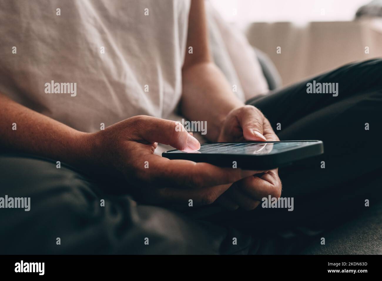 Donna adulta casual caucasica che usa lo smartphone a casa mentre si siede sul divano nel soggiorno, messa a fuoco selettiva Foto Stock