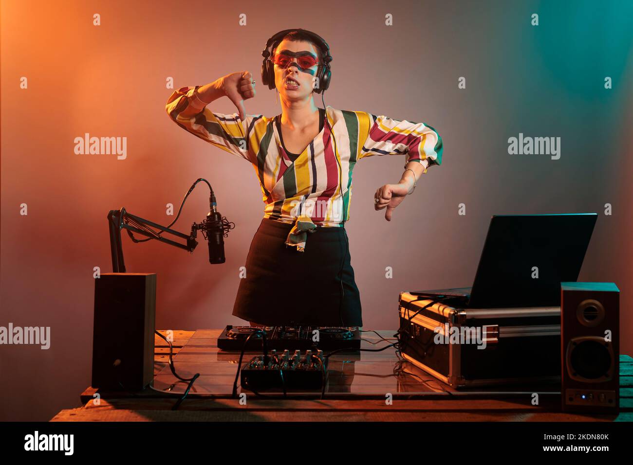 Musicista femminile che mostra i pollici giù segno in studio, facendo dispiacere e disapprovazione gesto dopo l'uso di giradischi e mixer per remixare la musica techno. Esprimere il rifiuto e il disaccordo alla parte. Foto Stock
