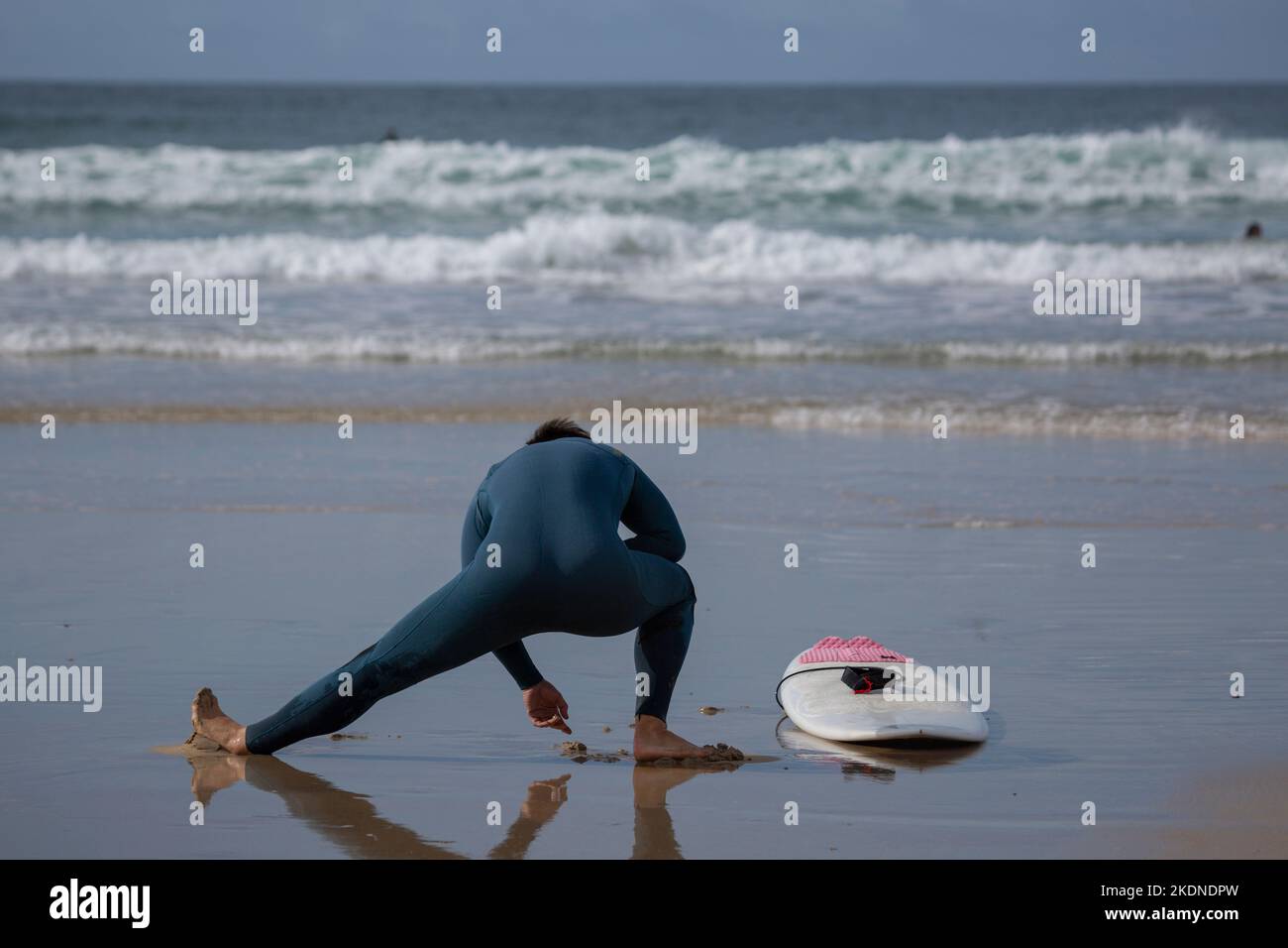 Un surfista con una muta verde e una tavola da surf bianca fa esercizi di stretching su Una spiaggia di Lanzada, o Grove, Pontevedra, Galizia Foto Stock