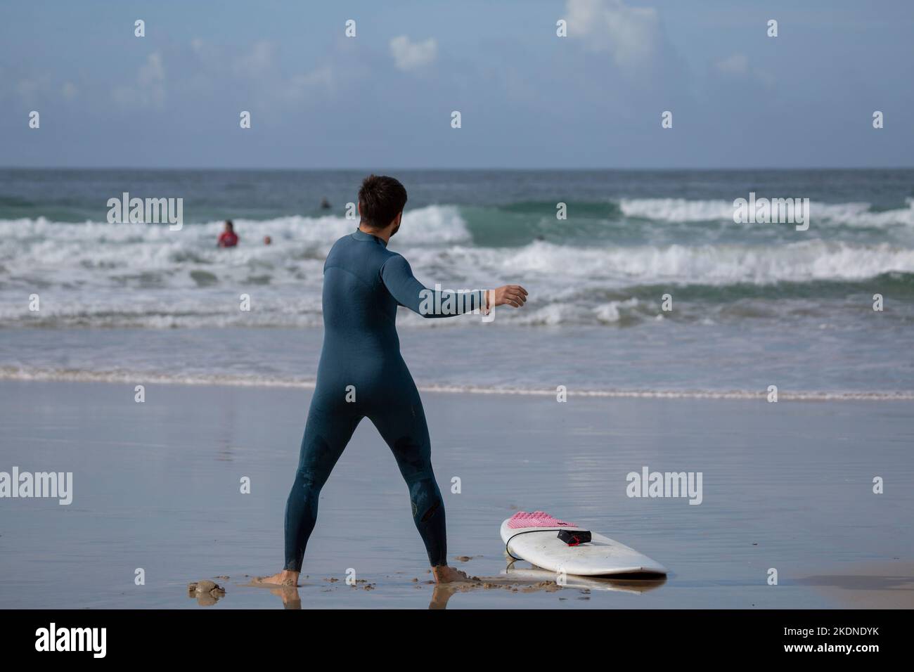 Un surfista con una muta verde e una tavola da surf bianca fa esercizi di stretching su Una spiaggia di Lanzada, o Grove, Pontevedra, Galizia Foto Stock