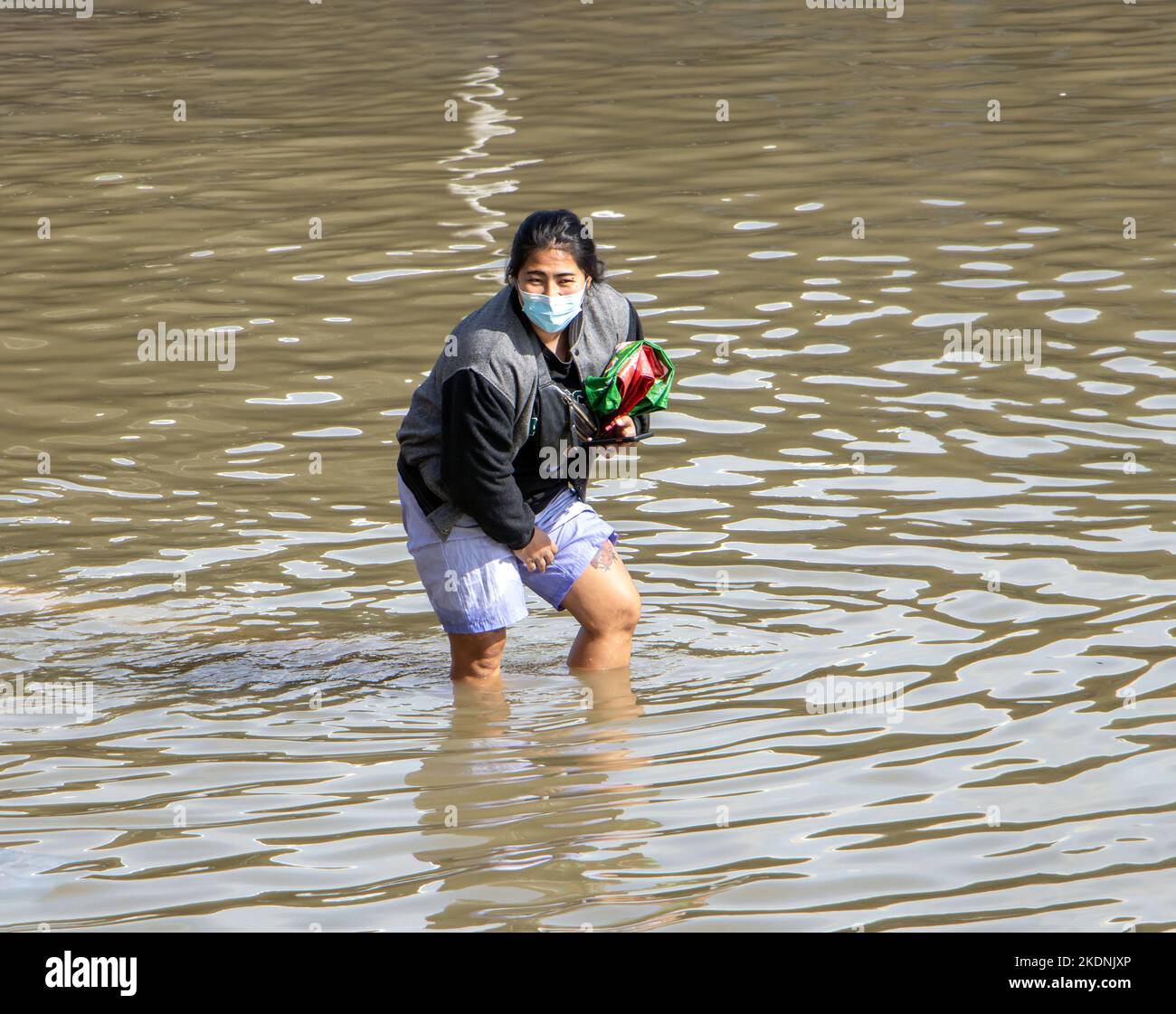SAMUT PRAKAN, THAILANDIA, ottobre 29 2022, Una donna arrotola i suoi pantaloni mentre cammina attraverso una strada allagata Foto Stock