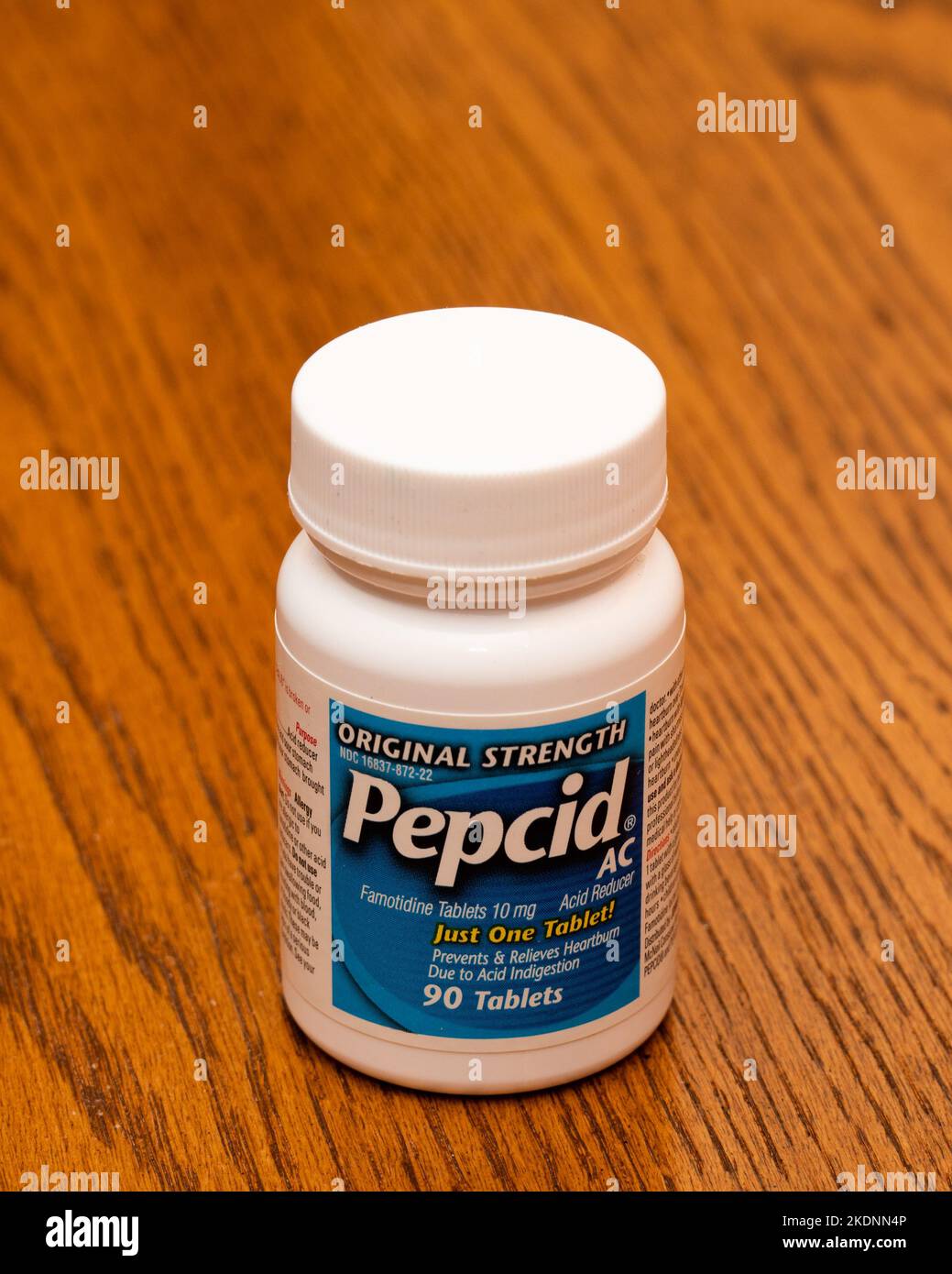 Una bottiglia di plastica bianca di Pepcid AC compresse per bruciore di stomaco, indigestione acida e mal di stomaco su una scrivania di legno. Foto Stock