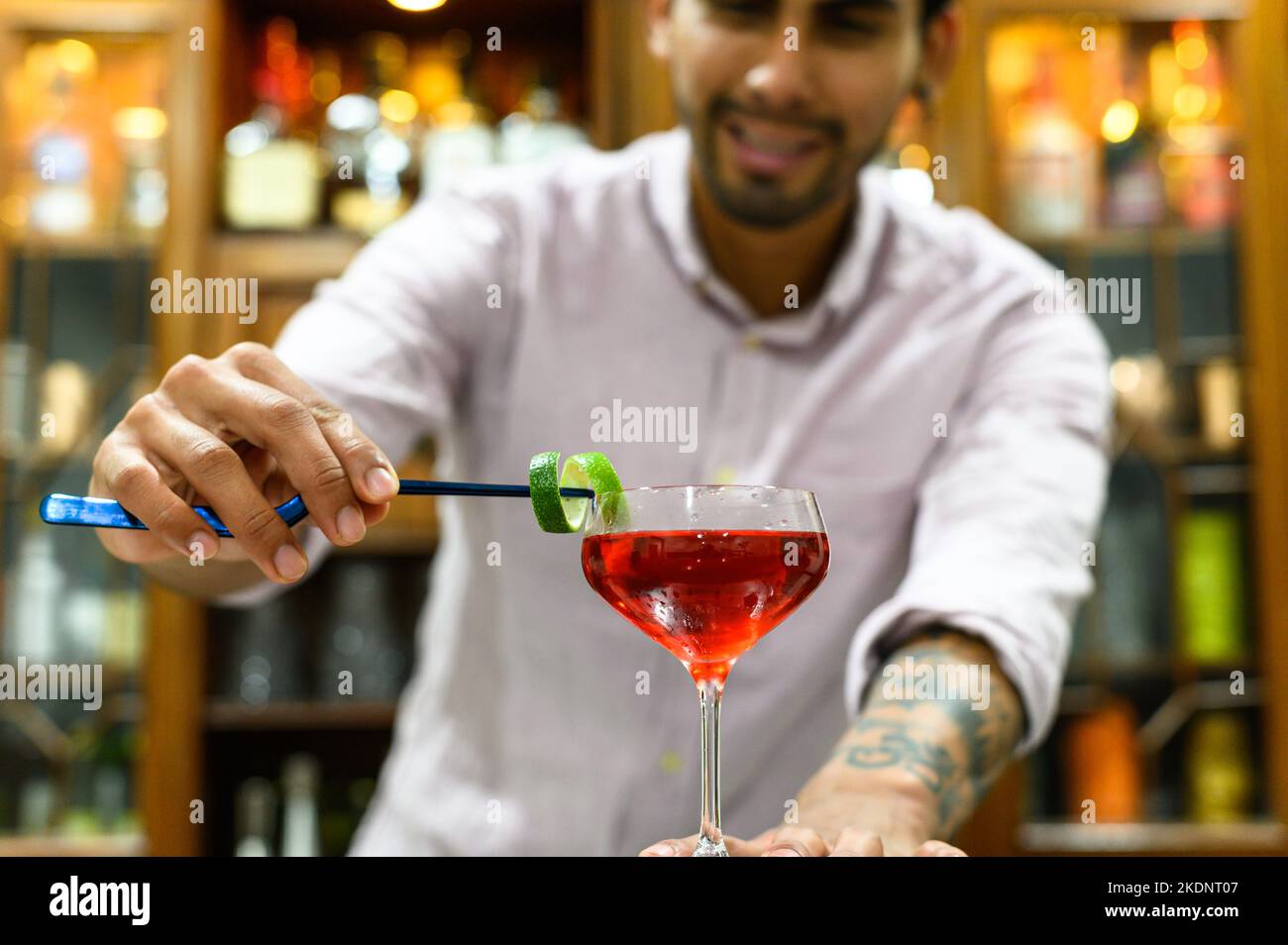 primo piano di bicchiere con bevanda rossa che barman accurata decorazione con buccia d'arancia Foto Stock