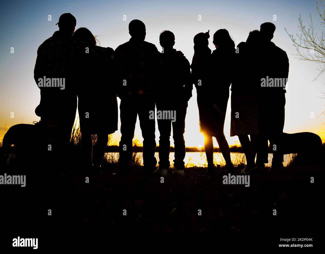 Silhouette di un gruppo di persone che guardano il tramonto di fronte ad un lago. Foto Stock