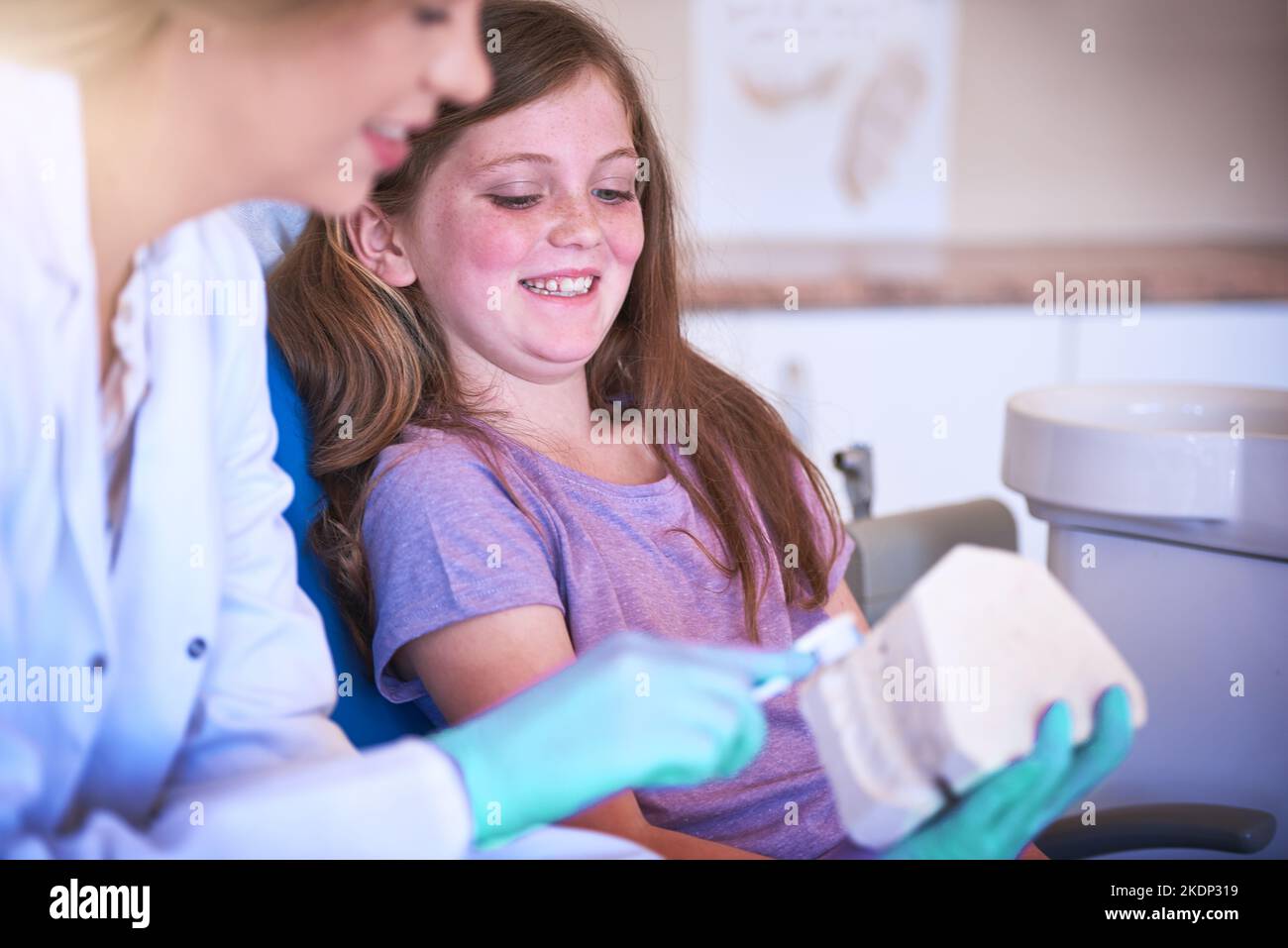 Non è mai troppo presto per iniziare a prendersi cura dei denti. Una dentista femminile che insegna alla sua giovane paziente come lavarsi i denti. Foto Stock