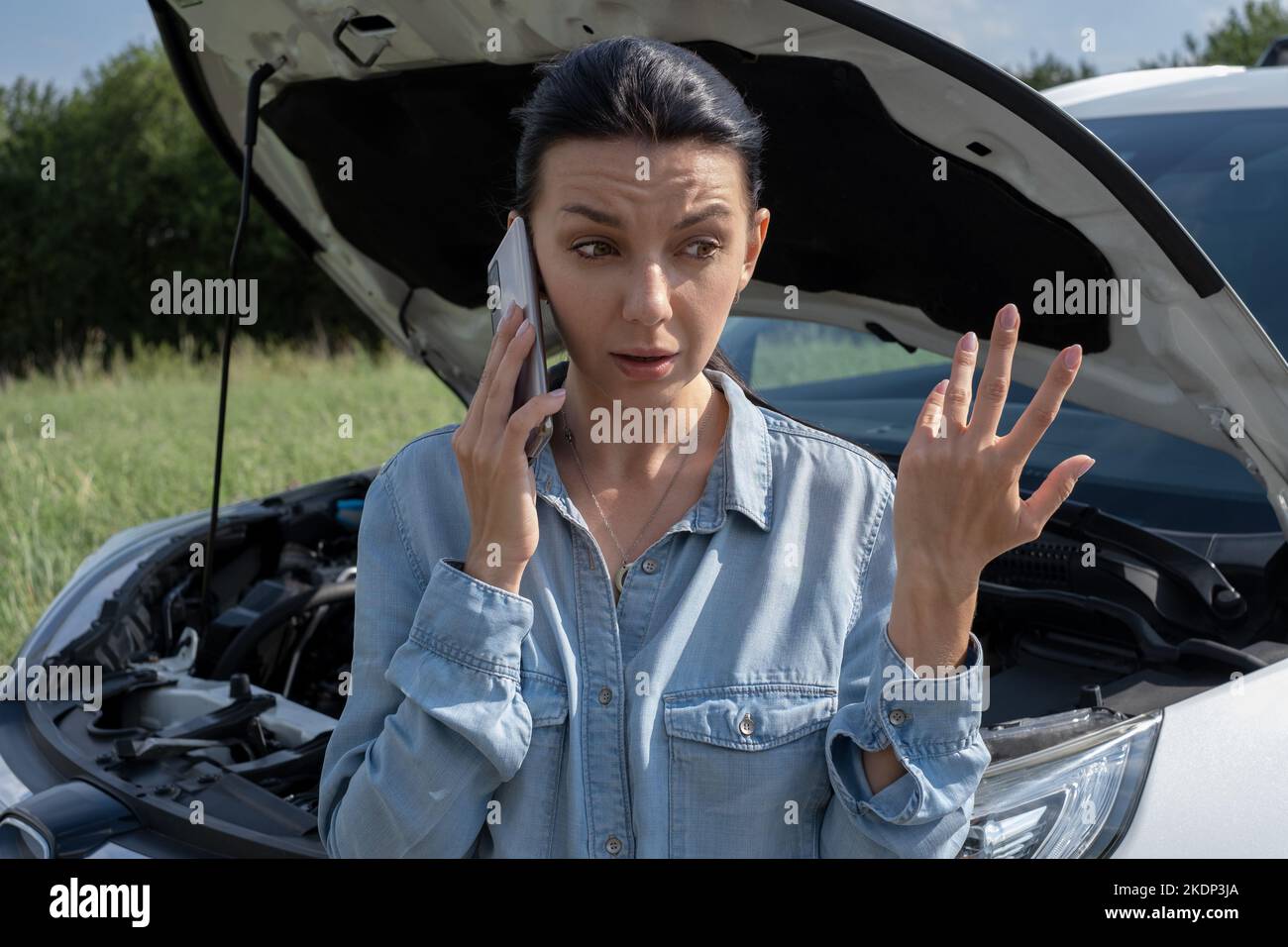 Giovane donna conducente in piedi vicino alla vettura con il cofano aperto. Femmina prima di un veicolo rotto e chiamata al servizio di riparazione auto. Emergenza sul paese r Foto Stock