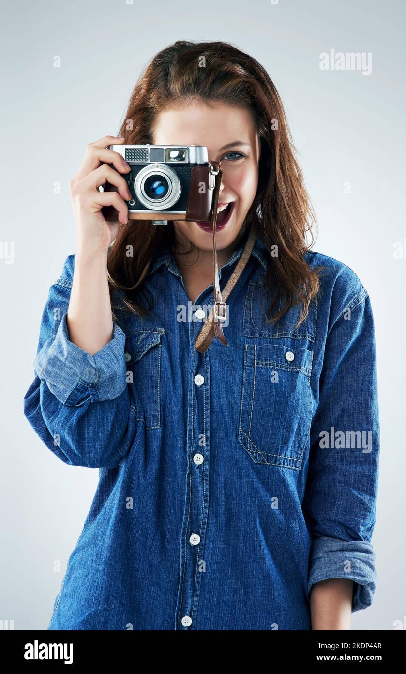 Mi piace congelare i momenti nel tempo. Studio ritratto di una giovane donna utilizzando una fotocamera vintage su uno sfondo grigio. Foto Stock