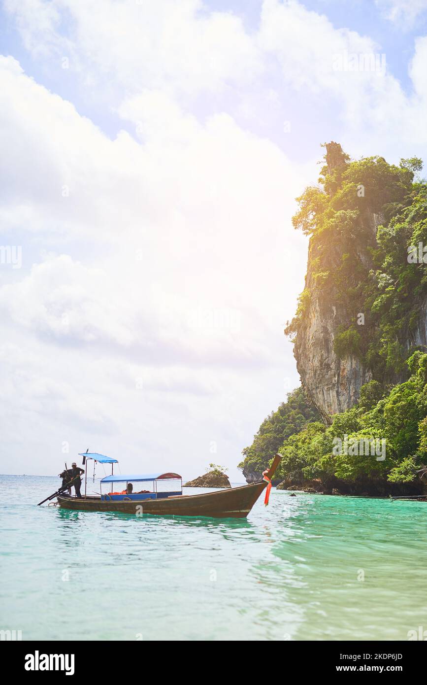 Un altro giorno in paradiso: Un uomo in piedi su una barca che galleggia in acque tropicali. Foto Stock