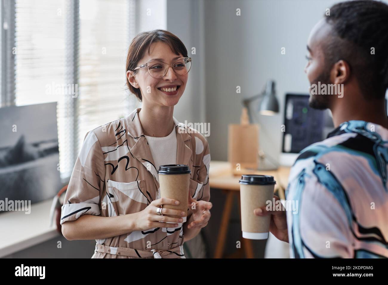 Girovita in su ritratto di giovane donna sorridente godendo il caffè da asporto mentre chiacchiera con il collega sul posto di lavoro Foto Stock